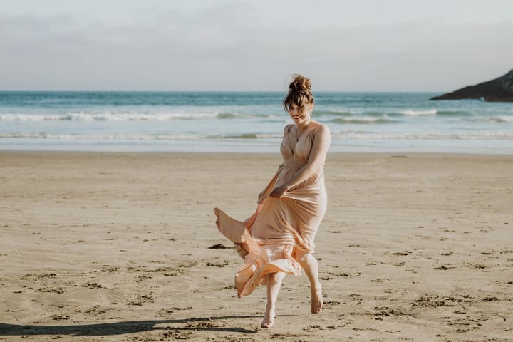 Beach front Tofino arranged photo shoot A couple posing on the rock, Videographer Brittany Ballamy running in the sand, surfer Emily Ballard sitting on the beach and a women in Reclamation company dress posing on rocks over looking the water 