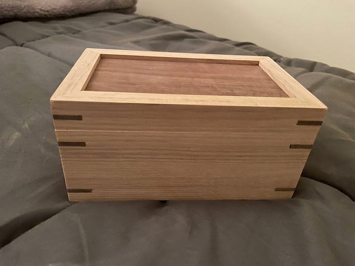 small two-tone wooden box resting on a gray comforter, first with lid on, then with lid off