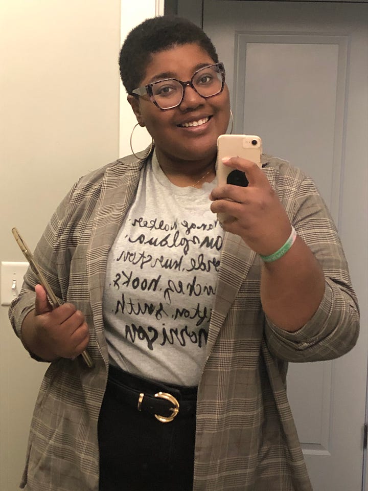 Image 1: Mirror photo of Ravynn in a lilac jumpsuit with a plaid blazer over it and a maroon scarf around her neck; image 2 is Ravynn in a maroon circle skirt and poet sleeve white blouse with a orange plaid cardigan over it and a maroon scarf around her neck and a purple beret on; image 3 is Ravynn in an Ironheart t-shirt, black blazer, and belted jeans; Image 4 is Ravynn in a feminist writers shirt with belted black jeans and a plaid blazer over top.