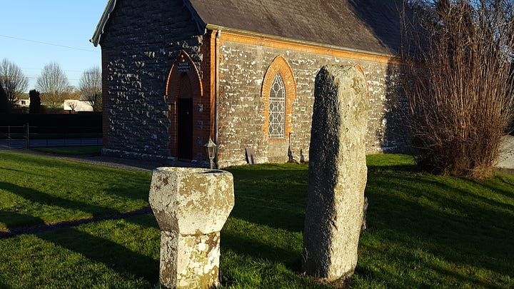 1. old font and standing stone in the graveyard. 2. The medieval tower. 3. Close-up of arched window high on tower wall with carved figure slightly above and to the left. 4. Zoom capture of the stone head with very weathered body barely visible.