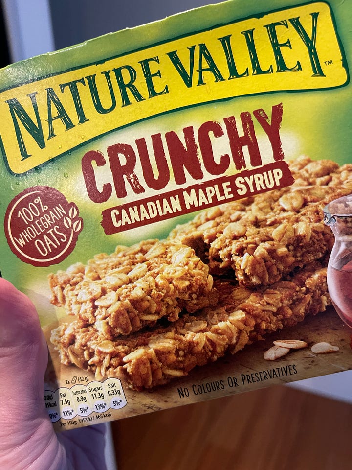 A box of Nature Valley Crunchy Canadian Maple Syrup granola bars and a bag of Bolo Lêvedo. 