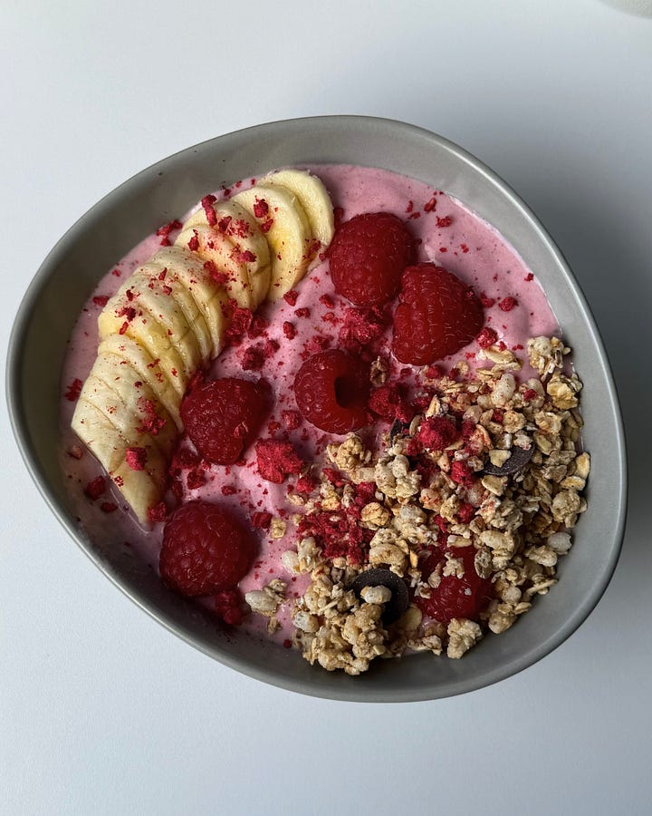 Thick raspberry smoothie bowl topped with fresh raspberries, chia seeds, and granola, served in a white bowl on a light background."Creamy blueberry smoothie bowl topped with granola and frozen blueberries, in a neutral-toned bowl with a spoon beside it."