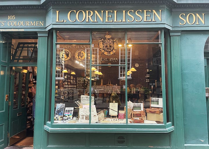 The frontage of the art shop Cornelissen's, a drawer of orange pastels, pigments in jars, and the Gosh Comic's window display for Pride - a rainbow made of comic book covers.
