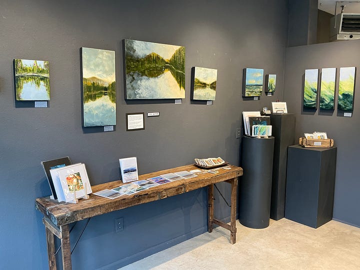 A gallery wall with multiple paintings of a lake reflection