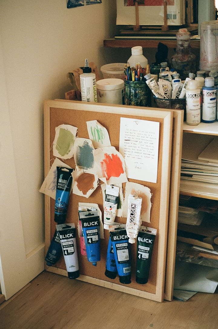 a quote about creativity under an original painting; a cork board pinned with paint swatches and tubes of acrylic paint