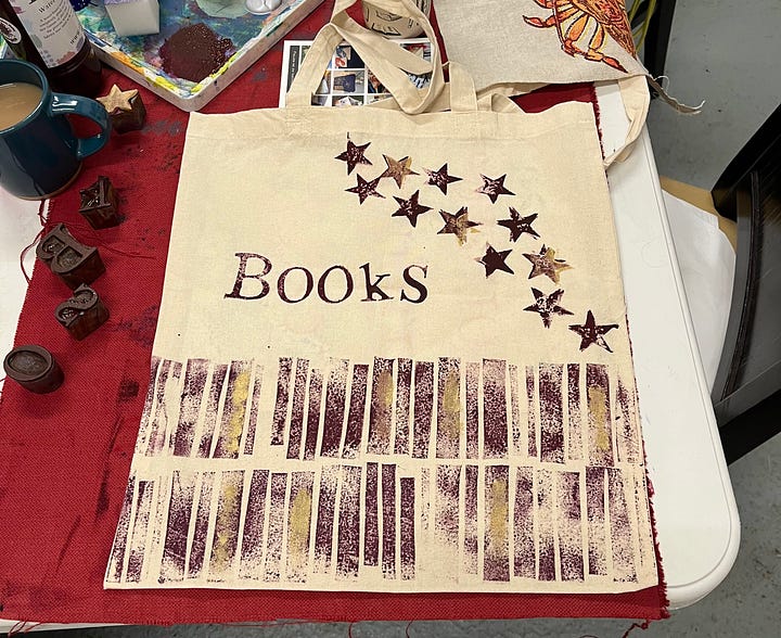 Hand-printed textiles; a tote bag with vaguely book-spine-ish pattern, the word 'BOOKS', and scattered stars; and a tea-towel with scattered green ferns and gold leaves, with one star in the melee. 