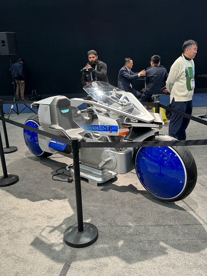 A super futuristic electric motorcycle, a woman in a cow suit being interviewed by me, and conference signs touting carbon capture, battery technology, and spray to extend food shelf life.