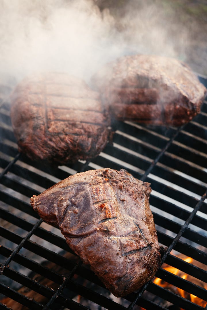 Clockwise from upper left: two men in front of open flame grill; man grilling on open flame; bison steaks on grill; squash on grill