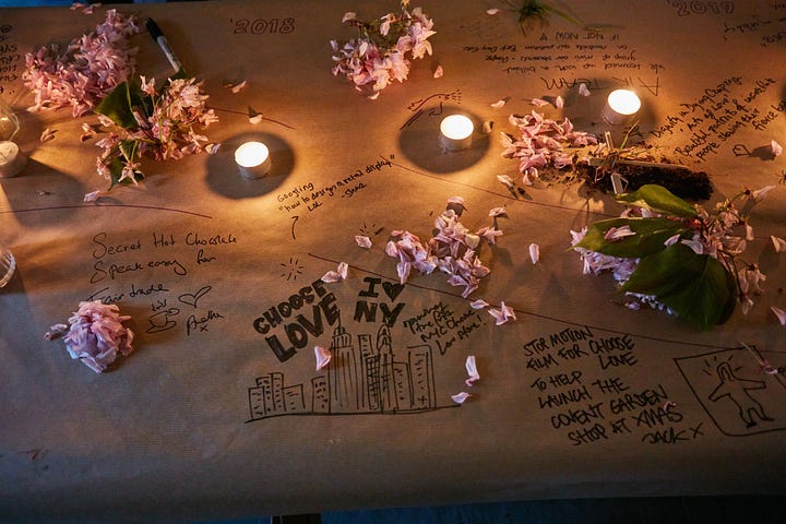 Two photographs of the Glimpse Farewell party. One a close up of the brown paper-covered table featuring hand-written notes and drawings of Glimpse memories, over which are sprinkled pink petals. There are three tea lights on the table too. In the photograph on the right, Glimpse's founder James Turner is standing smiling next to his colleague Ruth, who's mid-sentence as she recounts a Glimpse story. A male Glimpse guest is sat next to Ruth, looking up at her as she speaks. James is smiling..
