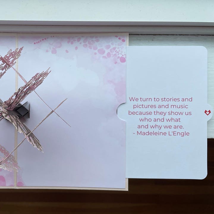 A pop-up cherry tree card featuring a quote by Madeleine L'Engle: "We turn to stories and pictures and music because they show us who and what and why we are."