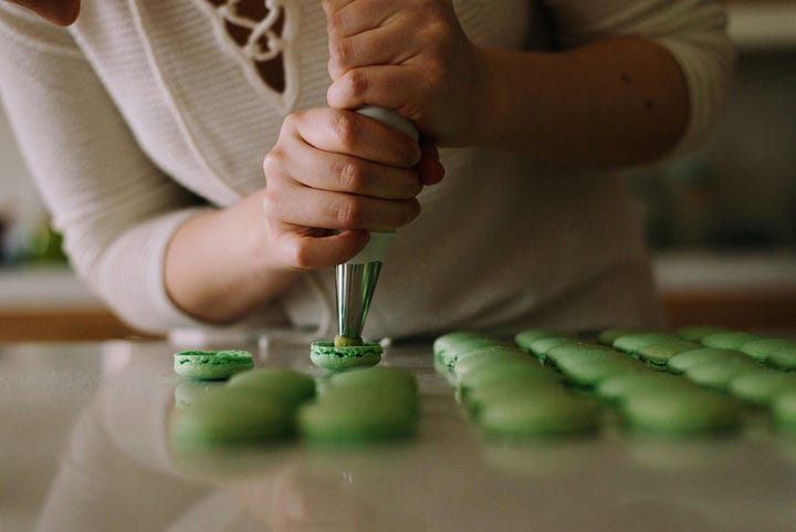 Left image is of golden spritz cookies beside a glass of milk; right image is of a woman using a piping kit to fill bright green macarons.