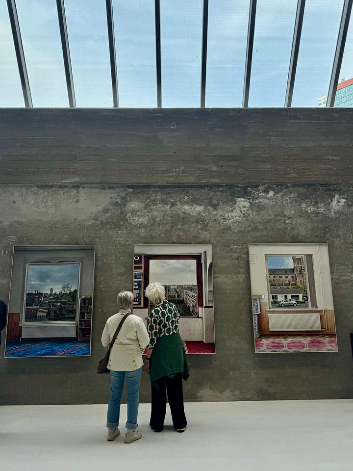 In the photo on the left, two women stand in front of a painting against a concrete wall. In the photo on the right, Katherine, wearing black, crosses her arms while standing in the industrial-style museum