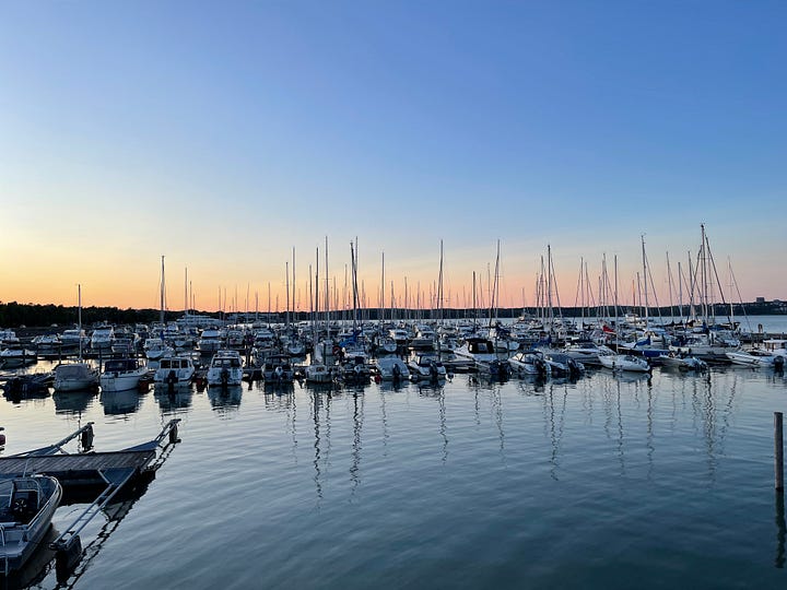 Still harbour water full of sail boats with a dark blue sky and orange light from the sun on the horizon