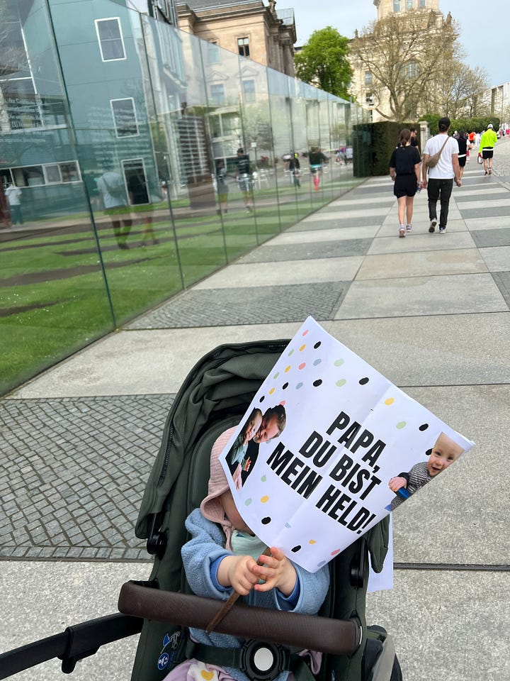 Auf dem ersten Bild ist meine Tochter Pippa im Kinderwagen mit einem Schild in der Hand „Papa, du bist mein Held“ und auf dem zweiten Bild die Laufuhr von Hannes mit der Aufschrift „Heute: Berliner Halbmarathon Berlin 2024, Training starten“