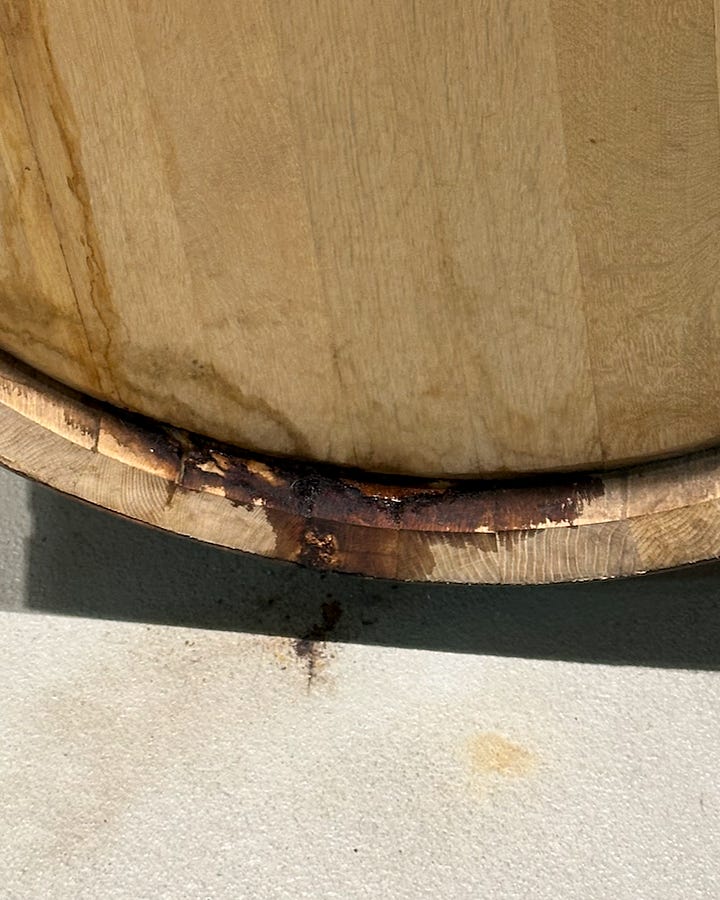Two close-ups of a wooden cask showing where the liquid inside has seeped through the wood and begun to leak out