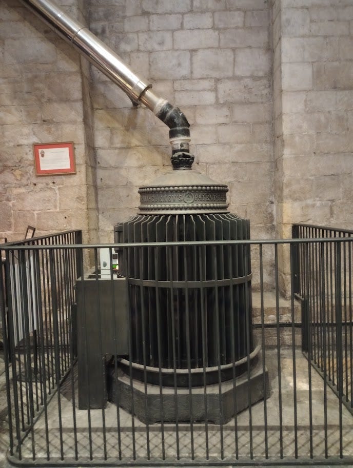 Large, cylindrical stove with slats, with pipe leading to ceiling