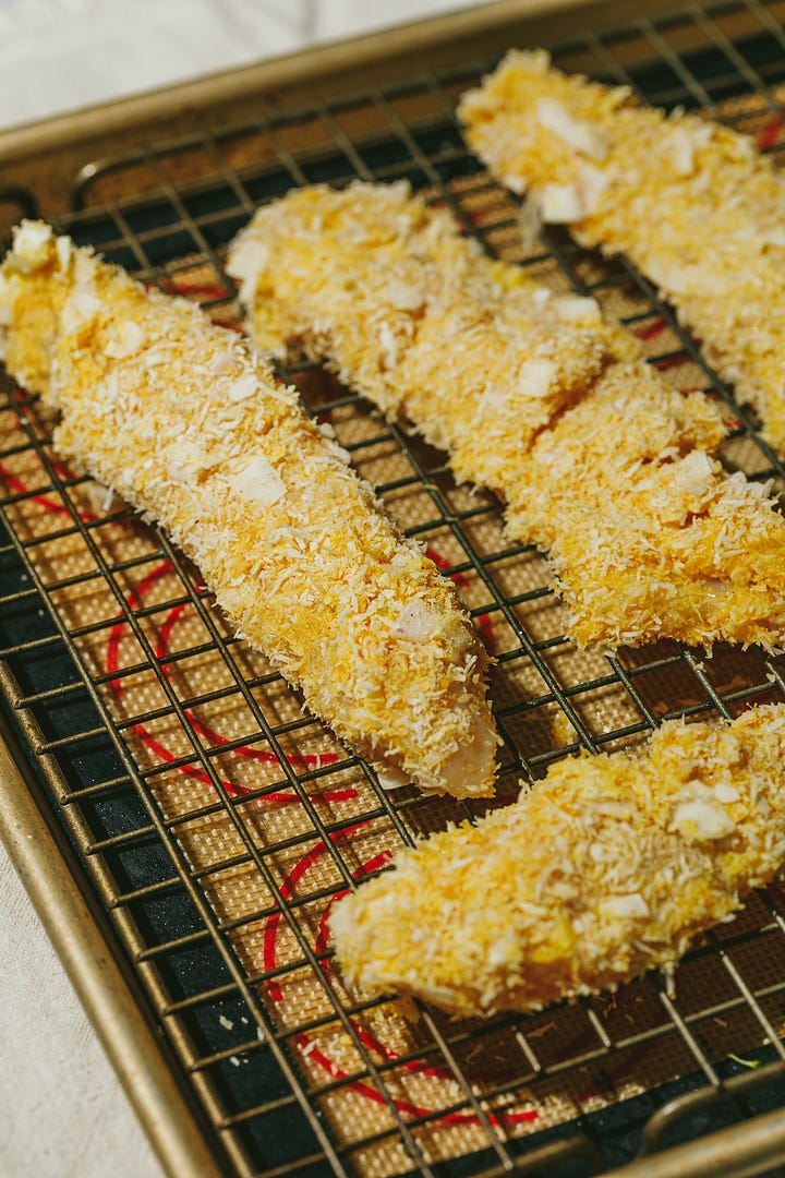 Coconut chicken tenders on baking sheet and on a serving plate. 