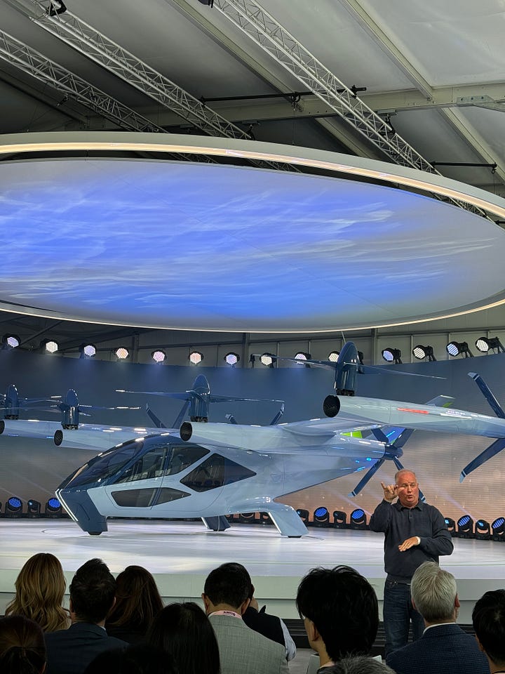 The Supernal S-A2, a sleek aircraft on a round stage surrounded by lights. One photo shows a green-lit interior with four passenger seats.