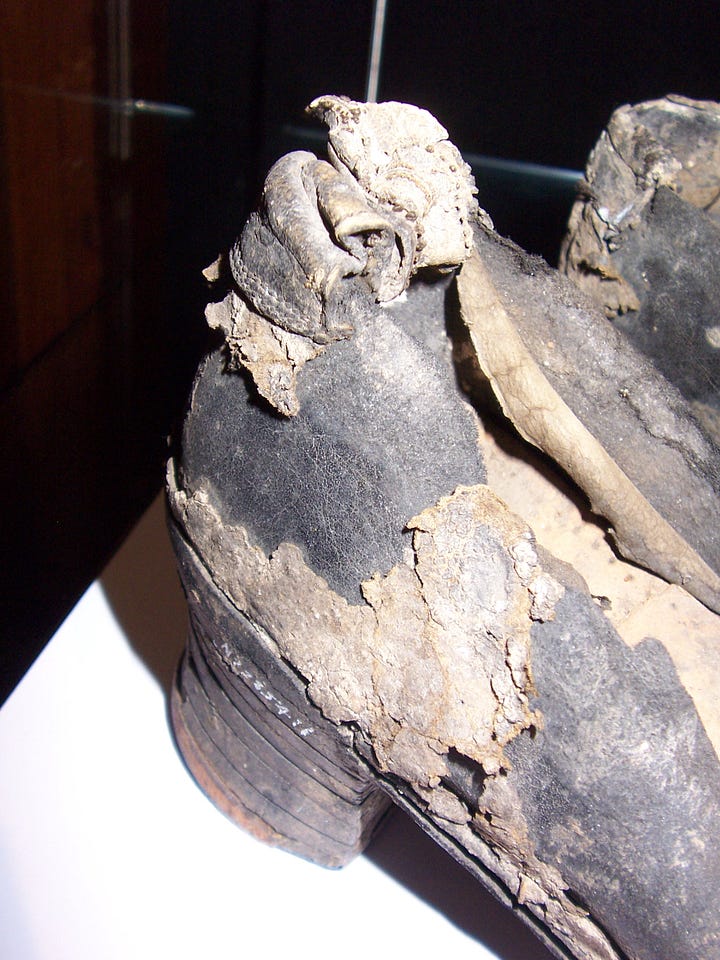 A pair of old shoes, partly decomposed, with patches of leather missing and flaked surface.