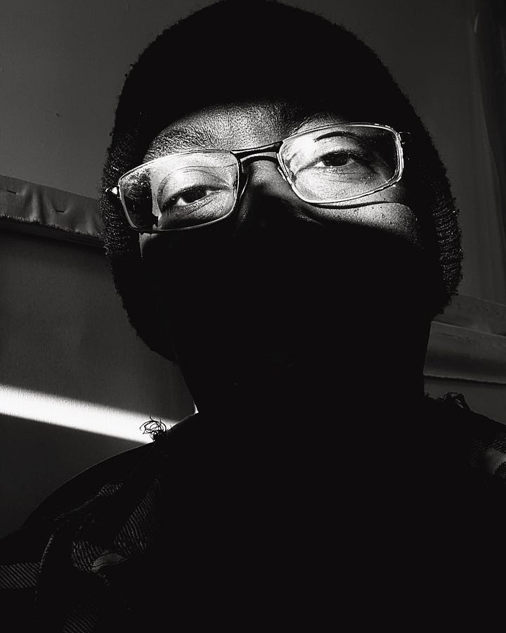 Two black and white photos of Tim McFarlane in his studio. Left: a shaft of light shows the artist's eyes and glasses and little else. Second photo shows the artist's full face, facing forward in a strong cylinder of light. 