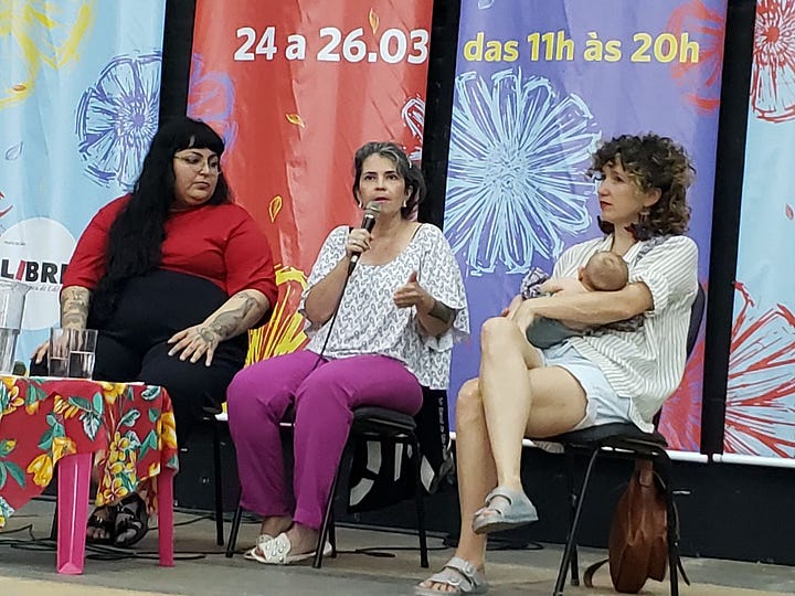 Foto colorida aberta mostra a feira de livros no Galpão do MST. Foto em close mostra as autoras palestrando, conforme explicarei no texto abaixo.