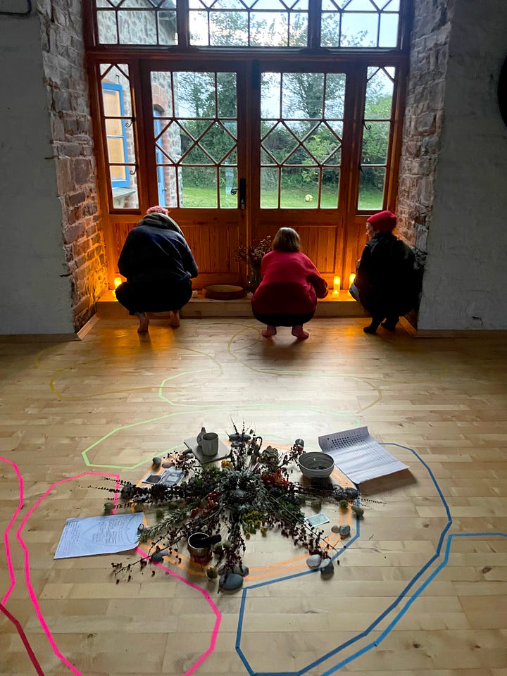 L-R: three white women and one Black woman sit on sofas and the floor writing in journals, with tissues, herbs and a jug of herbal tea in the foreground. A group of nine women stand in a circle on the lawn of a farmhouse, in the background. 10 women eating lunch around a farmhouse style table, with floral arrangements in the centre. Three women crouch on the wooden floor of a barn, their backs to us, lighting candles. In the foreground is a floral mandala arrangement. Four women clamber down a steep coastal path to the beach