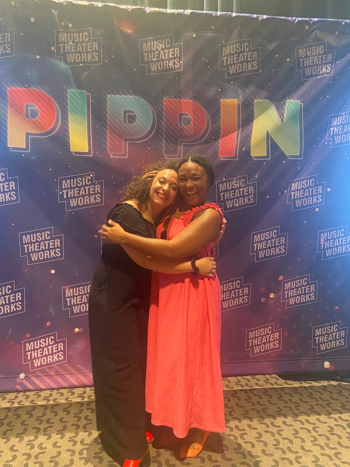 Left- Purple backdrop with the PIPPIN printed across the top in a rainbow ombre. The Music Theater Works logo (just those words outlined in two rectangles) cover the backdrop.) Sonia and Alexa are hugging. Sonia wears a black short sleeved jumpsuit with red close toed shoes, and has curly brown shoulder length hair. She is a light skinned black woman. Alexa wears a long pink sleeveless dress with orange closed toed shoes that are a bit pointier than Sonia’s. Her hair is in medium box braids, pulled back in a bun. She wears pink 70’s style retro sunglasses on the neck of her dress. She is a dark skinned black woman.   Right - A large room with white walls and worn glossy wooden floors. Some speakers and instruments in the background along with two men who are teachers at the school. Alexa and Sonia are sparring in their fight class at a conservatory in London. They are both lunging, pointing weapons at each other. The are wearing black leggings and shirts. (Sonia’s is short sleeved and Alexa’s is a scrappy tank top that she wears a purple sports bra under.) Alexa is facing away from the camera, and you can only see her back and side profile as she lunges with one weapon lower to the ground and one held high in the air. Her braids are in a loose ponytail that falls down her back. Sonia is in profile, but you can see her face. Both of her swords are held at the same level in the middle of her body. She wears an intense expression on hr face. Her hair is still curly, but a bit shorter. Her silver and pink sneakers are visible.