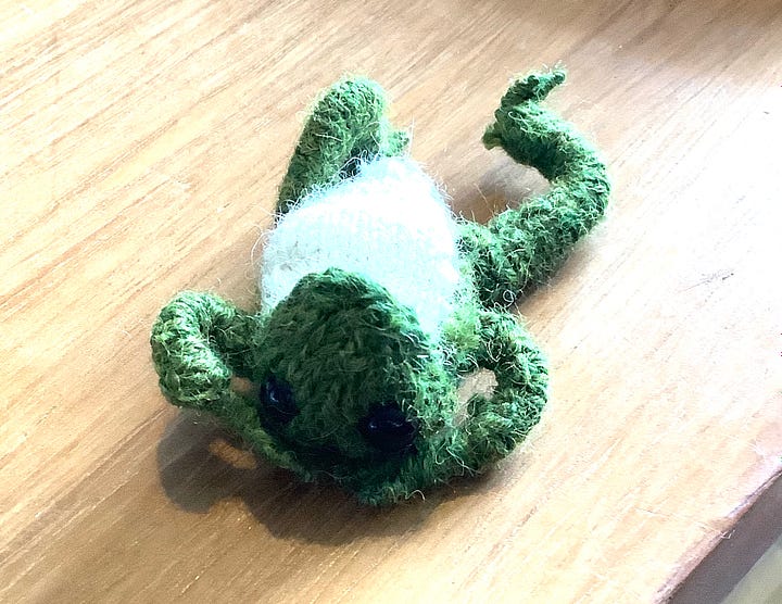 A green frog, with a cream chest, black eyes and a cheeky look. Sitting in a variety of positions, including lying on his back. 