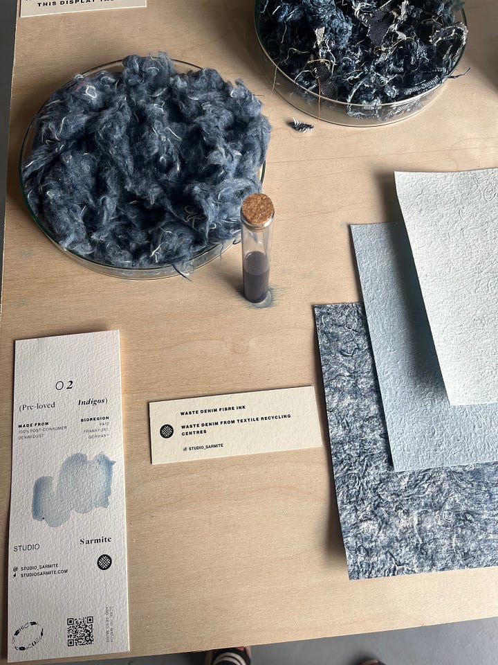 1-2. Exhibition table showing research artefacts for 'pre-loved indigos' from Studio Sarmite, including textile waste fibre, dye pigment, non-woven fabric sheets and information boards.
