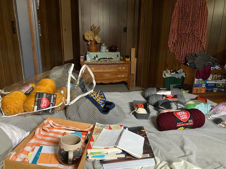 medium ginger shiba inu curled up in cosy chair, a crochet project in blue and gold, a pile of yarn skeins on the bed, same dog sat at the top of the house steps from behind