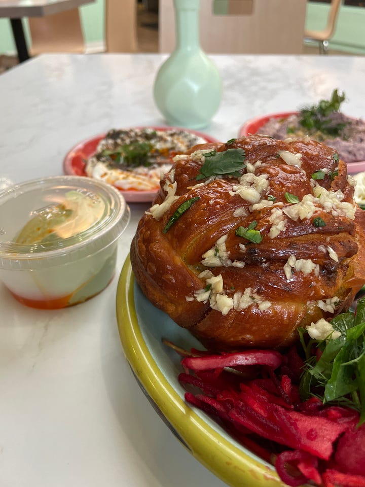 Bialy and dips, piece of lemon olive oil cake, hush puppies, a drink at a tropical-themed bar.