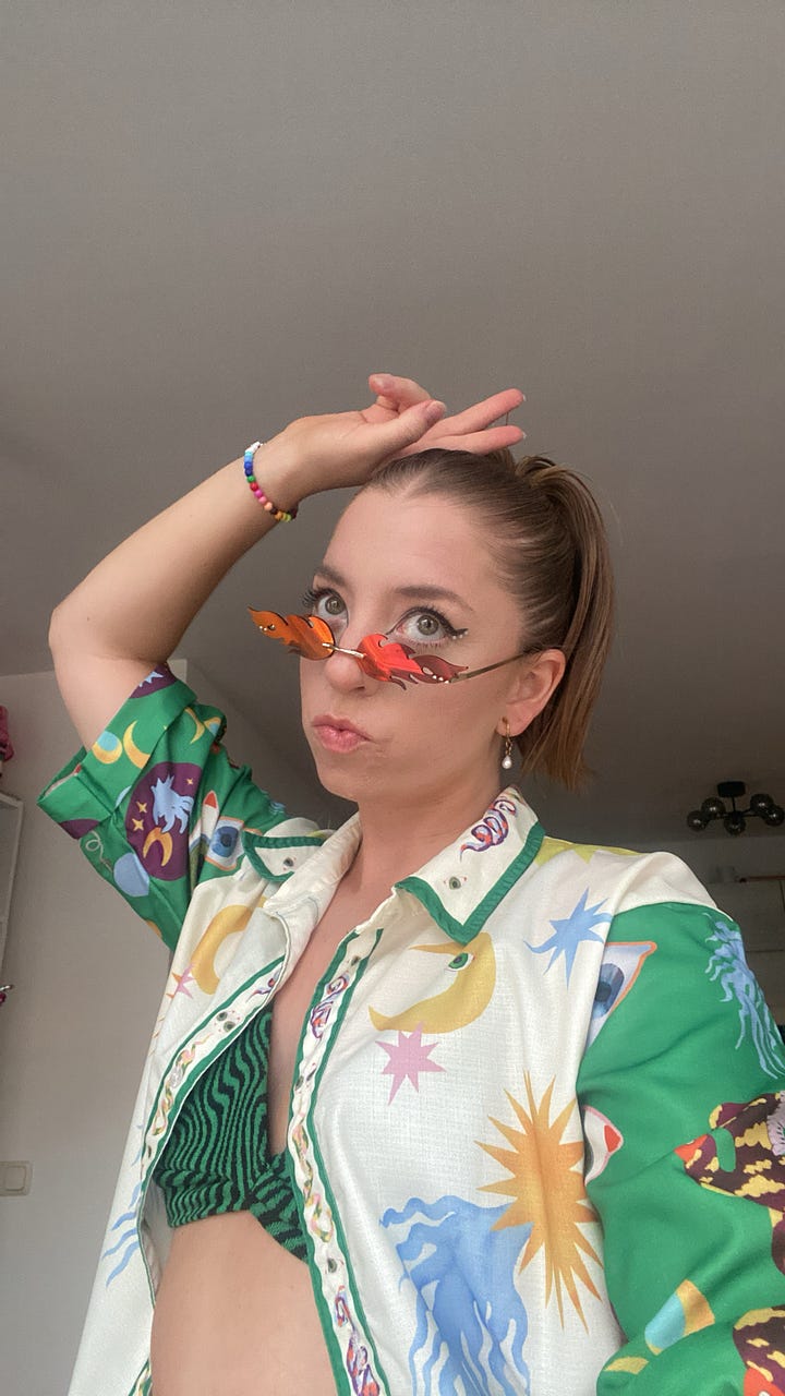 Left: Kelly in a yellow patchwork short sleeve button-up layered over a long-sleeve beige crop top with rhinestone tassels. Right: Kelly in a silky multicolored top and flame-shaped sunglasses.