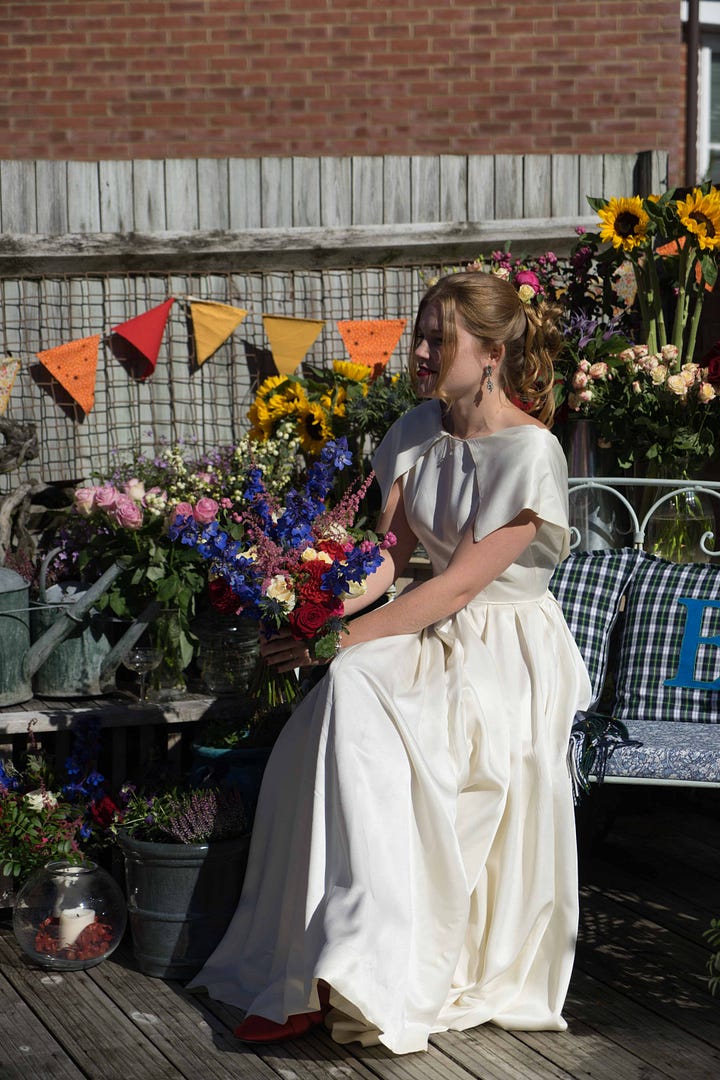 Libby in an ivory satin 1940s wedding dress carrying a bouquet of flowers and sat on a bench surrounded by flowers. Libby outside in a yellow vintage dress with short ruffled sleeves.