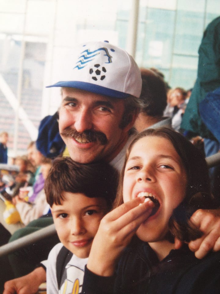 Father, son and daughter enjoying popcorn and a soccer game.