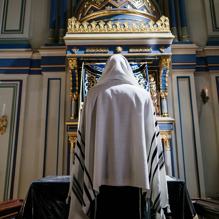 Left: open Torah scroll on reading table with silver crown behind; right, man with talis over his head in front of closed ark