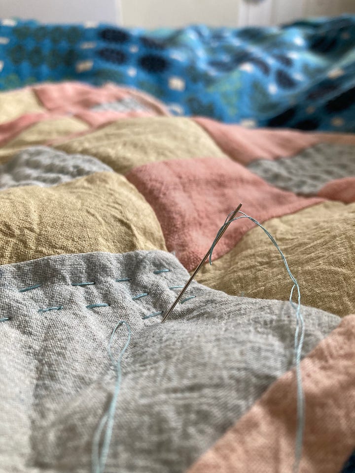 A needle sticks out of a mini patchwork quilt. 
