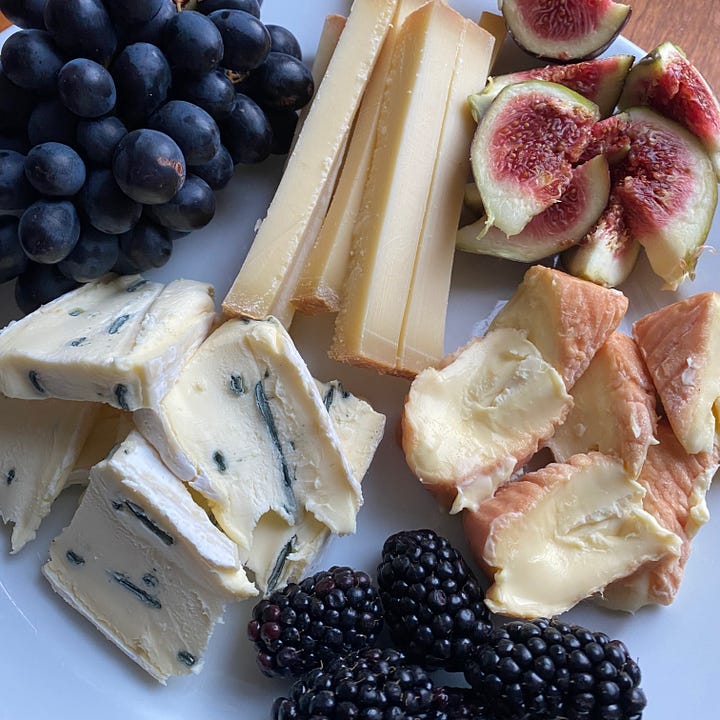 Selections of whole & sliced cheeses, some hard, some squidgy, some very ripe with ripe figs, blackberries and grapes