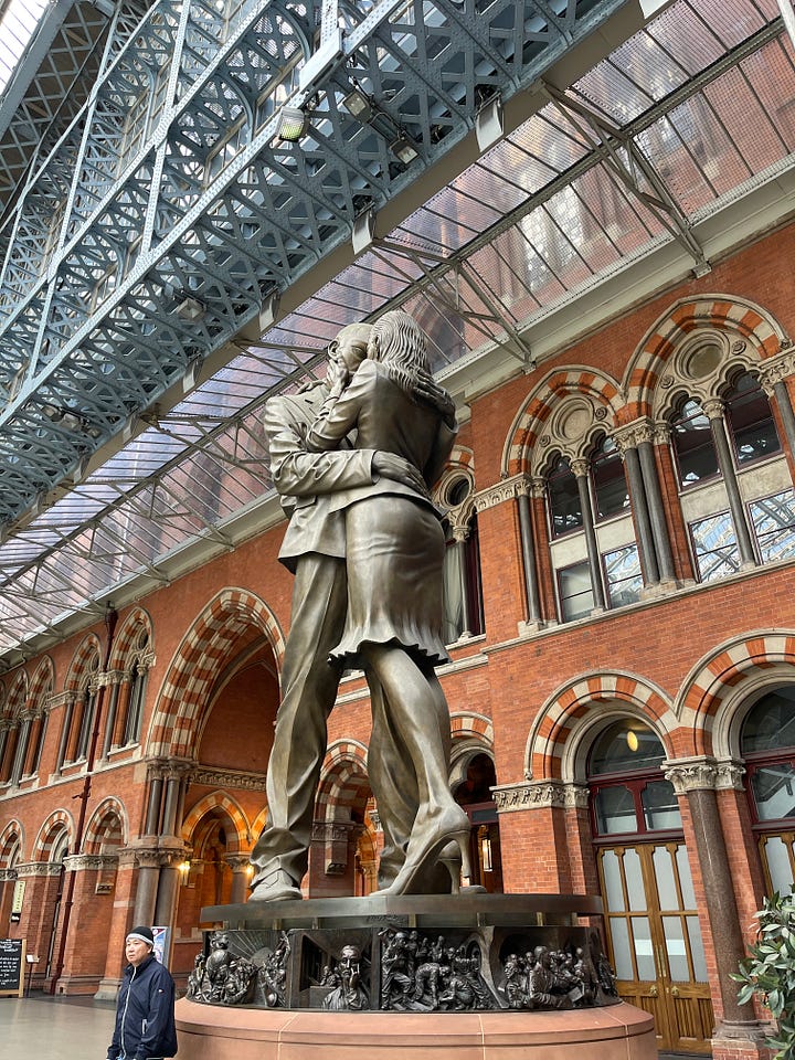 Outside image of the station, inside the station on the first floor, high vaulted glass roof over station end of line stops, a close up of a bronze statue with a half a face and a 3D tunnel and arches, photo of the large bronze sculpture of a man and women hugging 