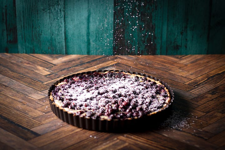 Sprinkling a blueberry custard tart with powdered sugar.