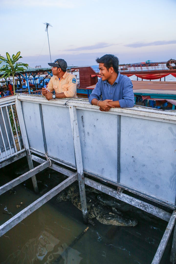 Various images from a day of photograph at Tongle Sap, including a man in a motorcycle helmet pointing, a boat in a river beside stilt houses, some kind of racoon animal in a cage, local children torturing shrimp, a man sitting on a railing, a young girl looking bored while trying to sell beer, and two men standing on a wall over a huge crocodile.