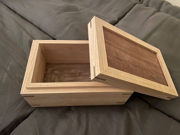 small two-tone wooden box resting on a gray comforter, first with lid on, then with lid off