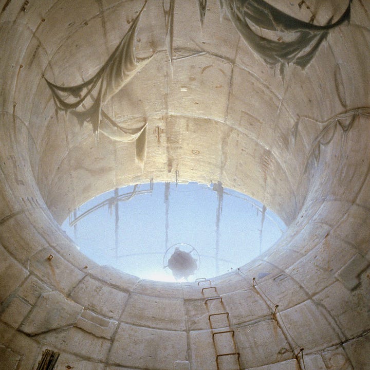 LEFT: Detail from LUMEN 5.1 featuring a man holding a large metal ring as he stands in the eye-shaped opening of an upward curving tunnel. RIGHT: Close detail from LUMEN 5.1 featuring curving textured wall. Rusty rebar forms a ladder up the curving slope. On the right, the paint of a yellow star chips and weathers. On the left a metal grate weeps lines of rust down the concrete.