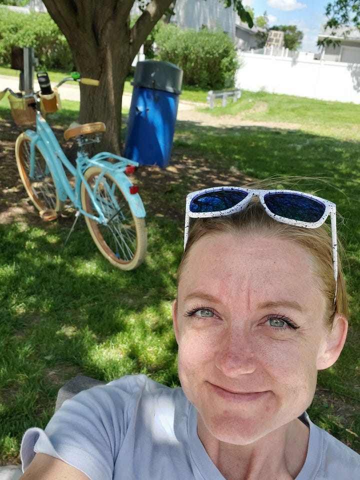 A mural with the words "Dream In Lilac" being painted; a human earthling by a bike