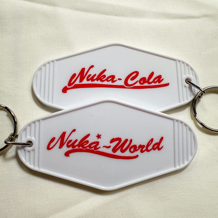 White hotel-style keychains with red text saying Nuka World and Nuka Cola