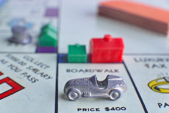 A Monopoly board with a car on Boardwalk with a green house and red hotel in the background; Jenga tower balanced precariously