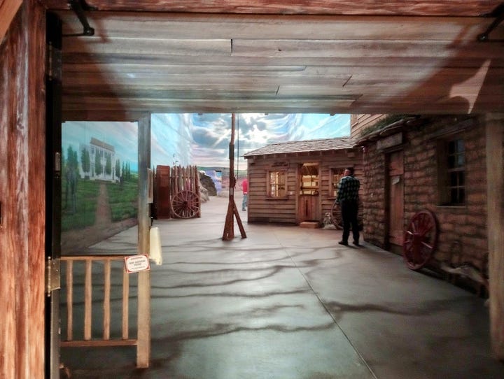 Photos showing log buildings and US flag on flagpole, swirly clouds and skies in high vaulted ceiling