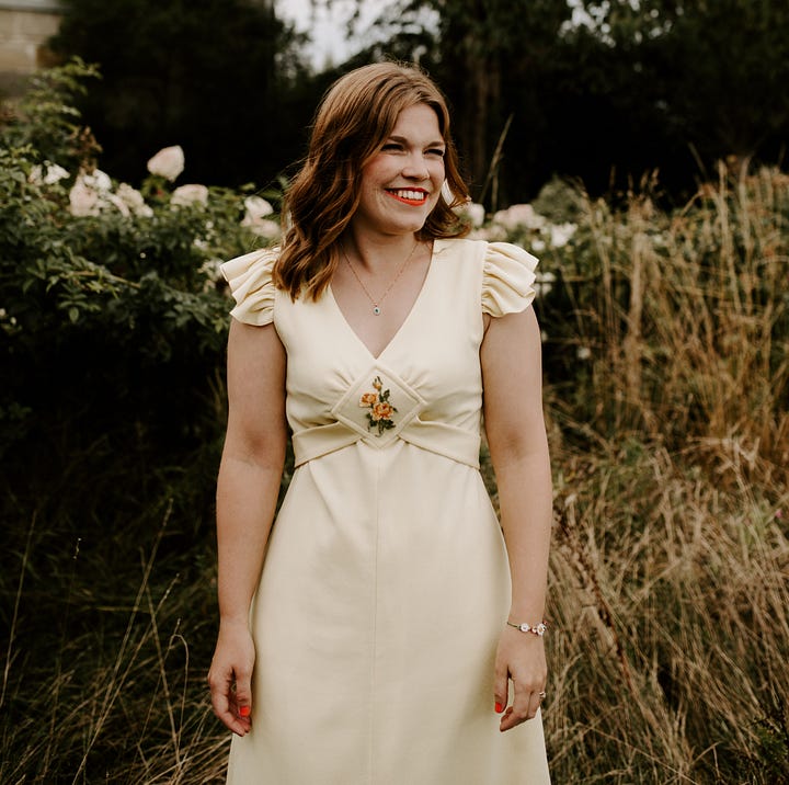 Libby in an ivory satin 1940s wedding dress carrying a bouquet of flowers and sat on a bench surrounded by flowers. Libby outside in a yellow vintage dress with short ruffled sleeves.