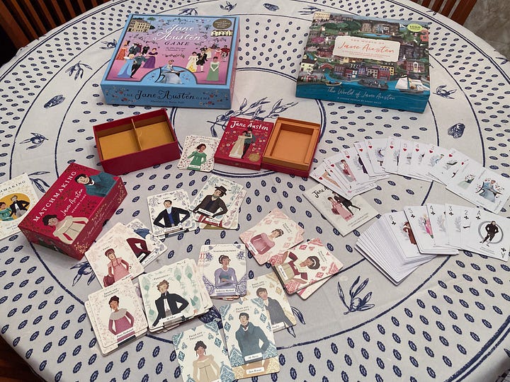 The boxes for "The Jane Austen Game," "The World of Jane Austen" puzzle, "Matchmaking: A Jane Austen Memory Game," and "Jane Austen Playing Cards." Image 2: The game board during a round of play for "The Jane Austen Game." The many pieces are assembled on the board. Image 3: The Emma Woodhouse character board and character cards during a round of play of "The Jane Austen Game." Image 4: Cards from both "Matchmaking: A Jane Austen Memory Game" and "Jane Austen Playing Cards" are spread out on a table next to "The Jane Austen Game" and "The World of Jane Austen" puzzle. Image 5: A close up of the cards from "Matchmaking: A Jane Austen Memory Game" 