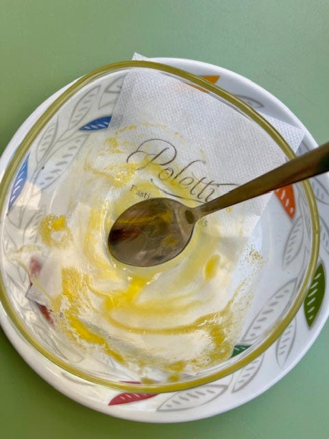 a ball of bright orange mango gelato in a clear bowl on a white plate with blue, red, orange, yellow and white leaves and a silver spoon and then the empty bowl afterwards