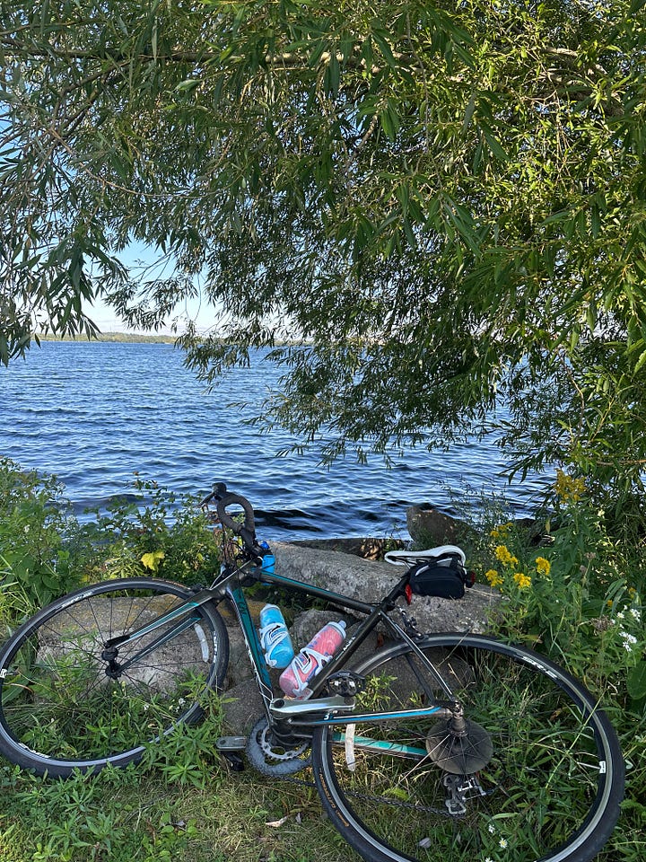 Bike lying on a rock by a lake. Kayak point floating into the sunset.